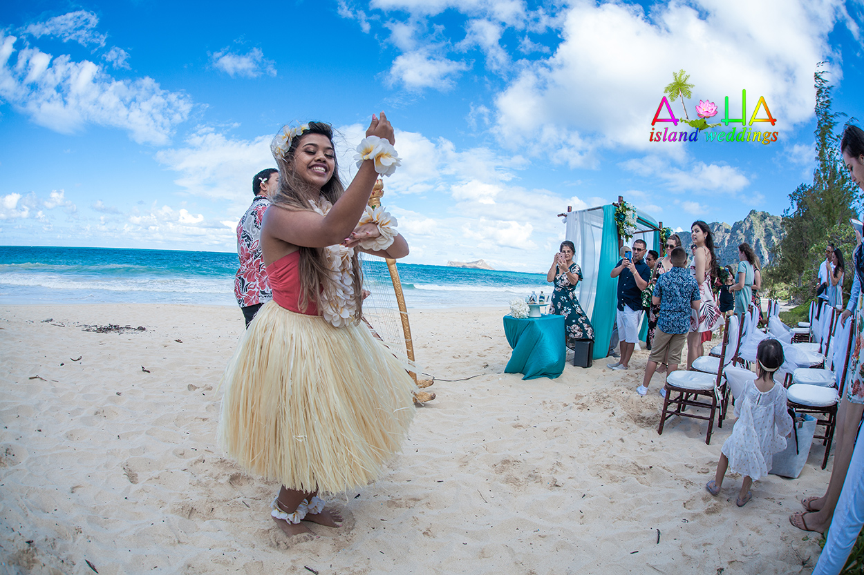 Hula dancer in a grass skirt dancing for the bride and groom on the sand